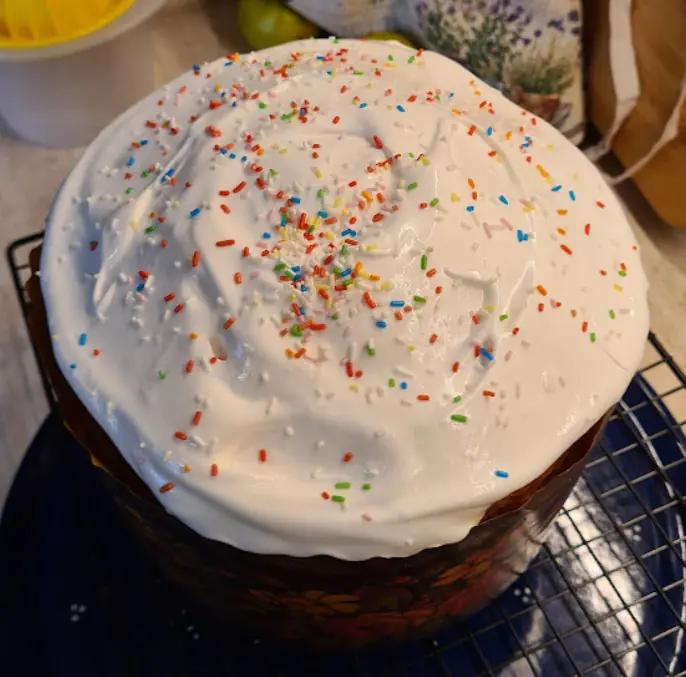 A paska covered in white glaze and sprinkles, cooling on a rack