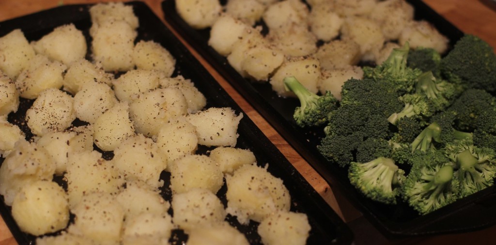 Potatoes and broccoli in cast iron roasting trays for roasting